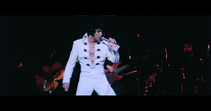 Elvis Presley performs on stage in a white suit