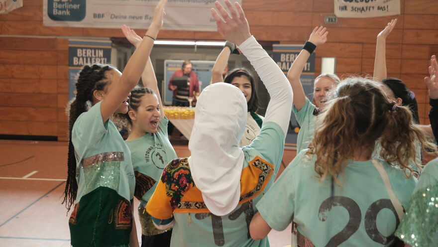 A group of school ages girls in sports uniforms raise hands in the air joyfully