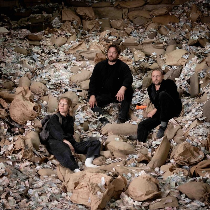 Three people sit on top of a gigantic pile of money.