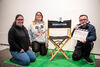 Three members of Options in Life group posing with a Director's chair and clapper board