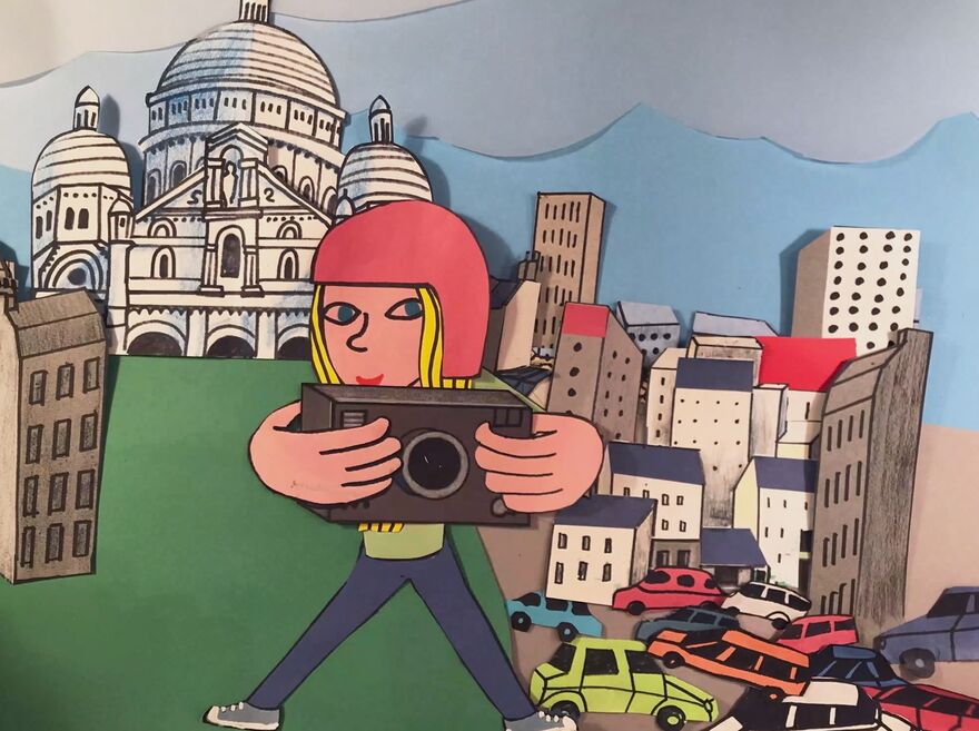 Papercut illustration of a girl holding a camera in a busy city. 