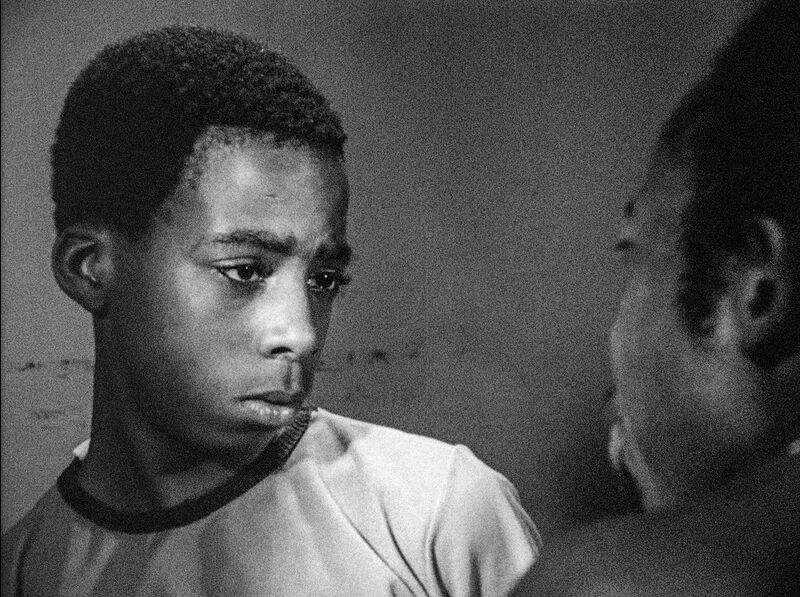 A young black man stares intently at another man who is just in foreground of the image