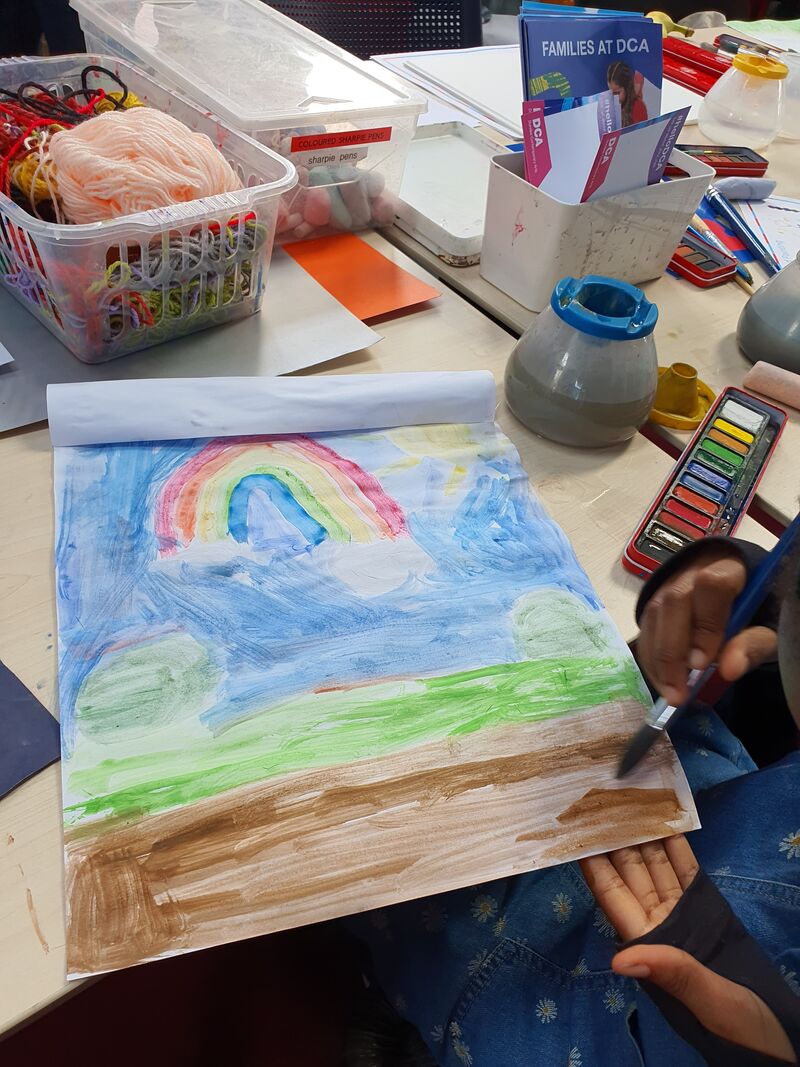Child painting a landscape with a rainbow