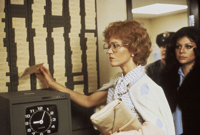 A woman in glasses carrying a purse punches her timecard