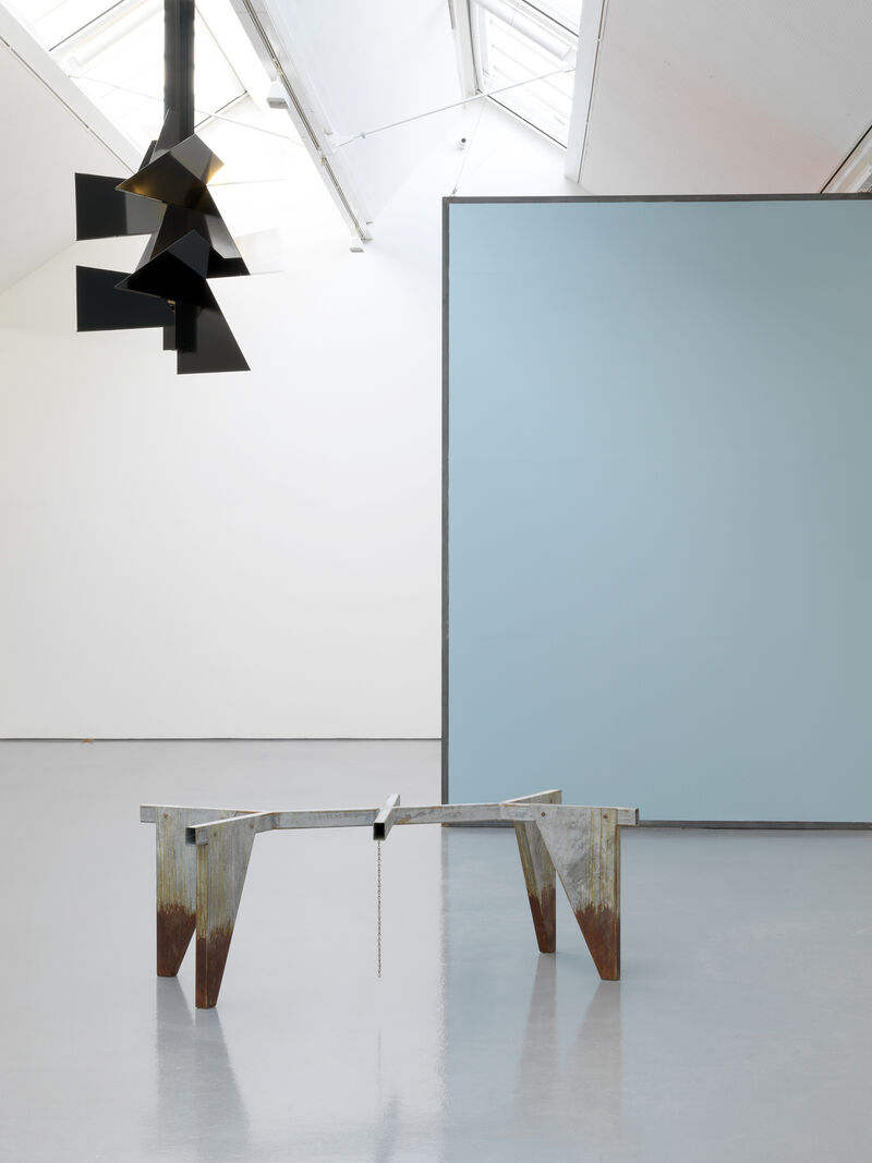 From Martin Boyce's exhibition in DCA Galleries. A triangular, black light structure hangs from the ceiling. There is a large, blue canvas in the background. An angular, metallic statue sits in the middle of the room.
