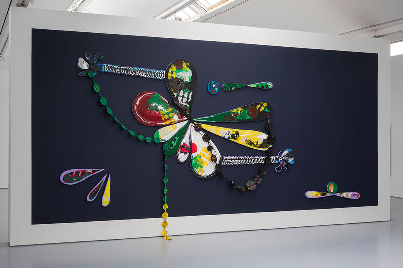 The image shows a mural with 3d elements, large petal shaped forms in yellow, green and white mostly, on a dark blue background. 