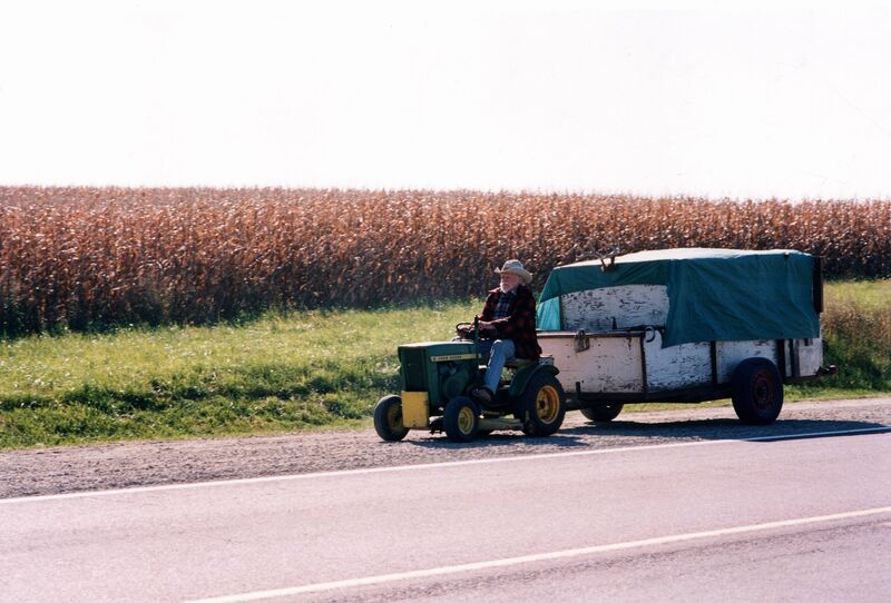 A man rides a tractor, pulling a large trailer, along a wide open road.