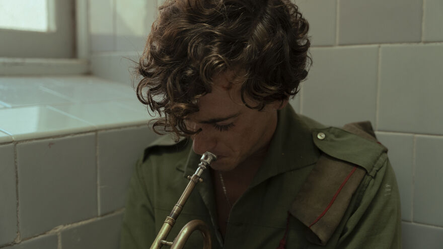 A man sadly plays a trumpet in a tiled room