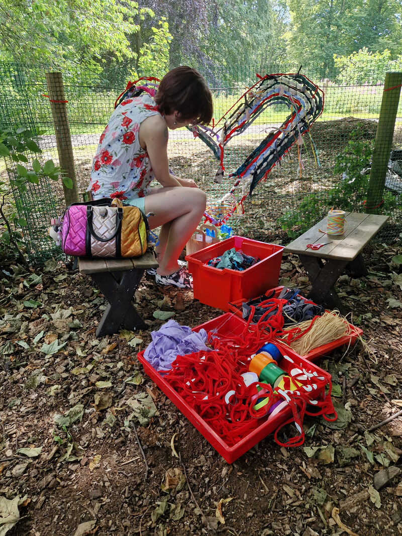 Person adding yarn to a heart artwork on a fence