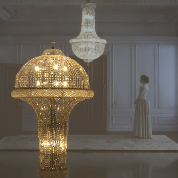 Works by Matthew Buckingham - a golden, sparkling chandelier reflected in a mirror, a black plinth, and the same chandelier again, this time in a room with a woman in early 20th-century clothing on.