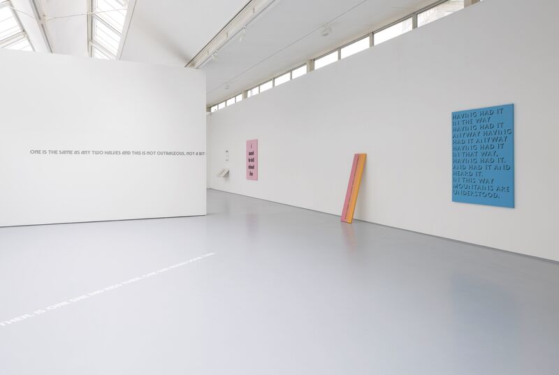 From Eve Fowler's exhibition. A blue canvas on the wall says 'Having had it in the way having had it anyway having had it anyway having had it in that way. having had it and had it and heard it in this way. mountains are understood'. Grey text on the wall says 'One is the same as any two halves and this is not outrageous, not a bit.'