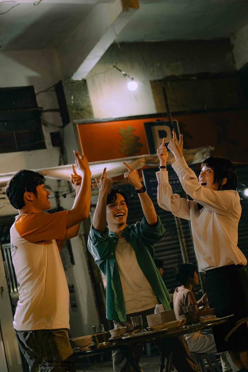 Three people dance and celebrate around a table.