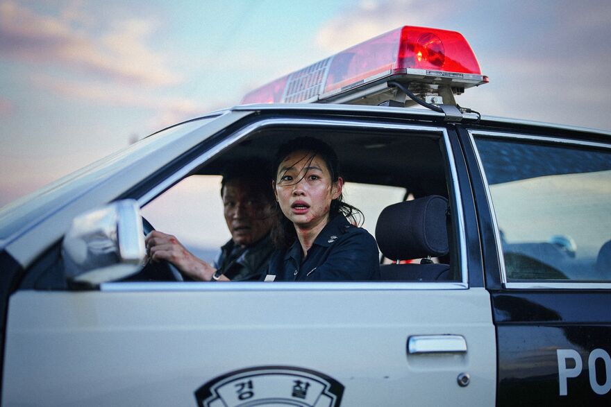 A female Korean police officer looks in horror from her car window