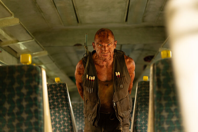 A bald man covered in iodine stands in a dirty train carriage