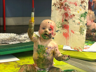 Baby covered in pain holding up a paintbrush