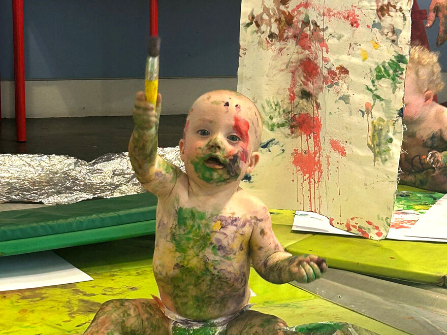Baby covered in pain holding up a paintbrush