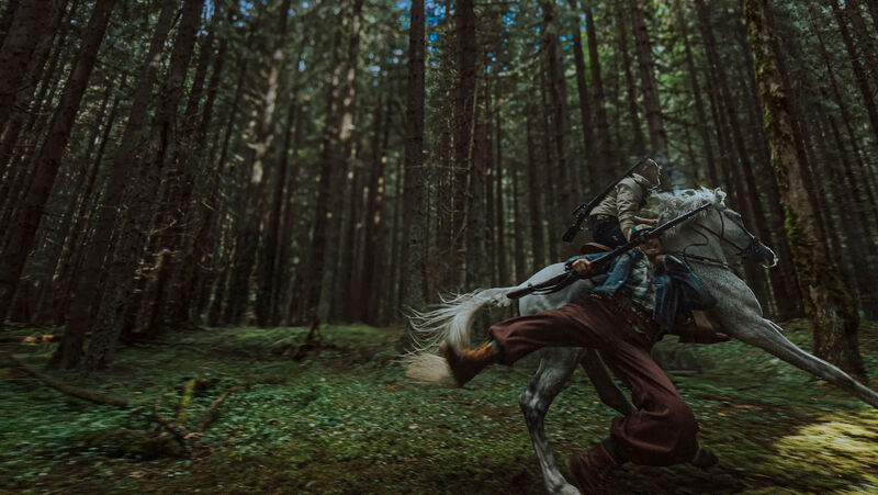 A man rides a horse at speed through a forest