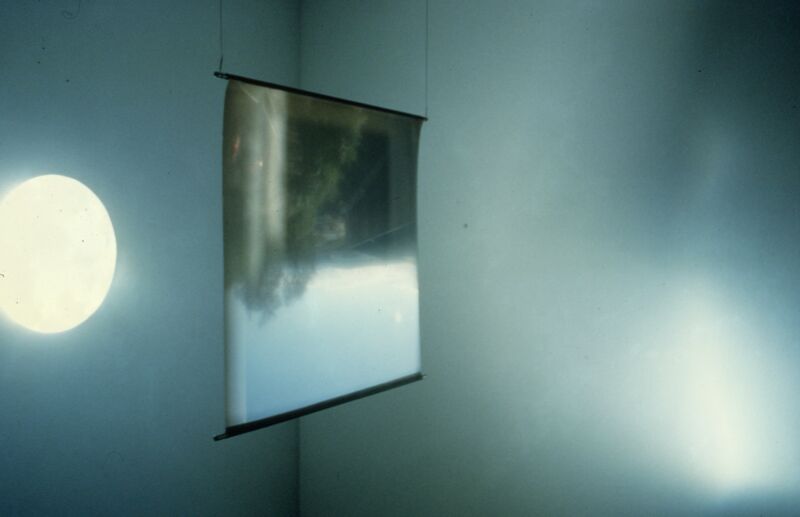 In a white room, a bendy reflective surface hangs from the ceiling.