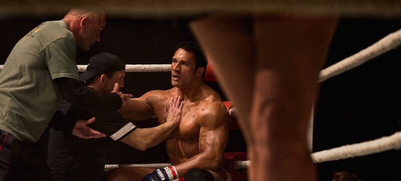 An MMA fighter sits in the ring while his coach puts his hand on his chest.