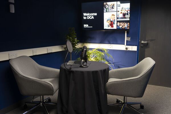 DCA's media suite, which features two chairs, a round table, microphone and large television display.