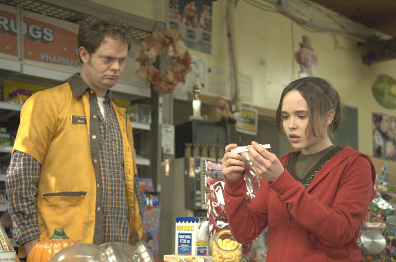 A girl looks in surprise at pregnancy test result while a man in a yellow uniform looks on