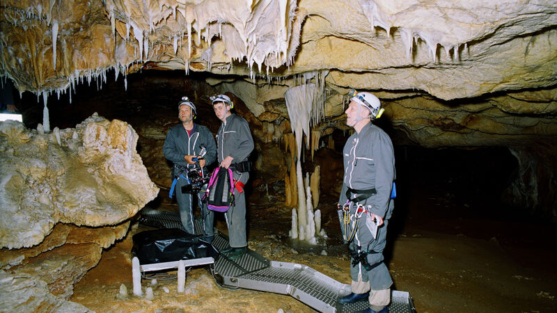 Three men in hard hats explore a dark cave