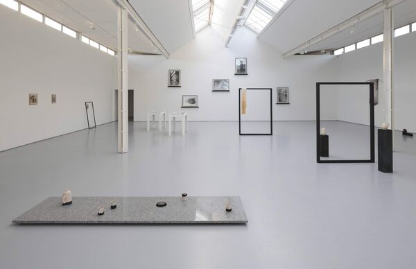 A still from 'Pieces of You Are Here'. A white gallery space is filled with pottery, stones and empty black frames.