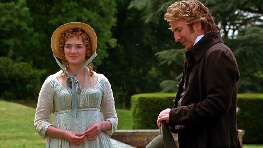 A woman with blonde hair wearing a regency dress stands outside smiling at a man.
