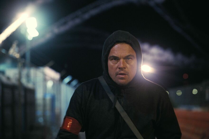 A man stands in a dark street wearing a dark hoodie with the hood up.