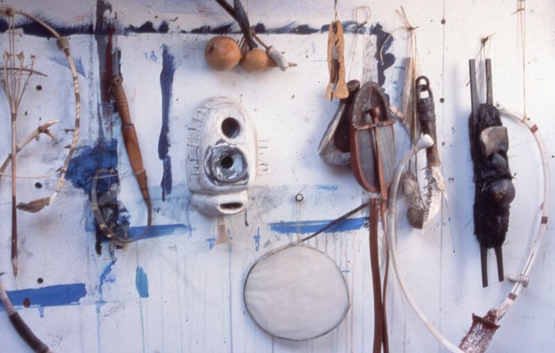 Abstract objects pulled from the sea hang on a white wall which is splattered with blue paint.