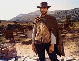 A man stands in a poncho and hat, smoking a cigar in the Old West