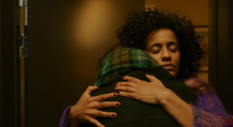 Two people hug each other next to a door.