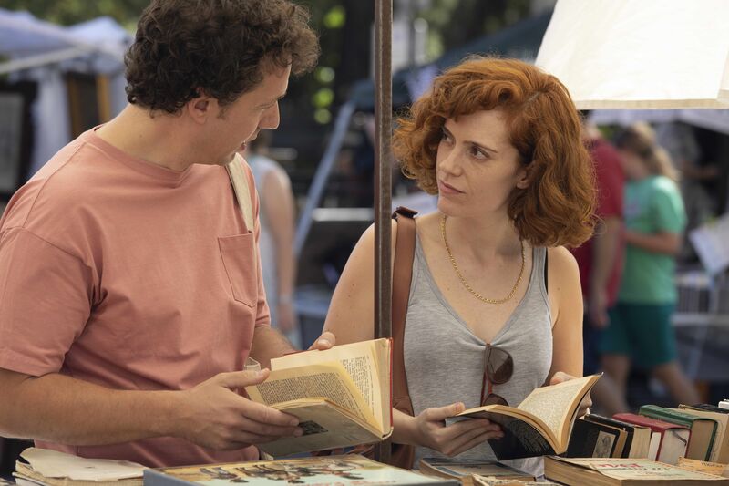 A man and woman look at books together at an outdoor market.