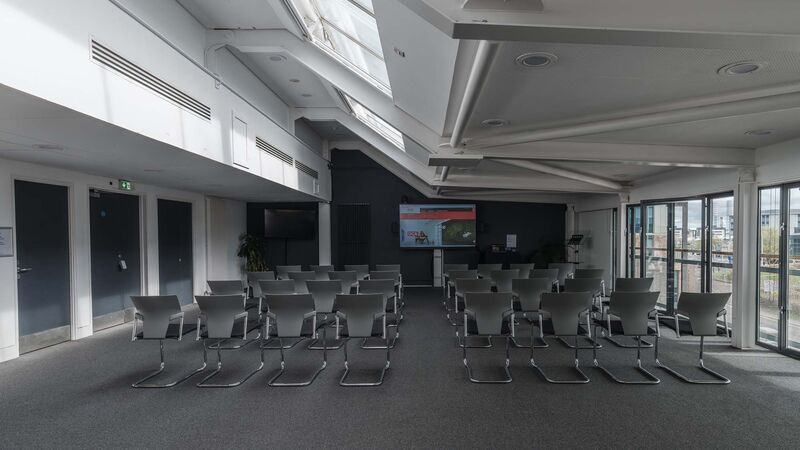 A meeting room with rows of seats and a screen, photo taken from behind