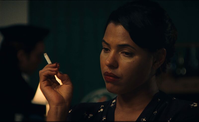 A woman with red lipstick smokes a cigarette in a dark room.