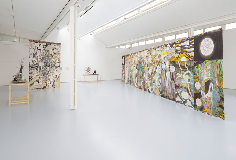 An installation image showing large hanging artworks in muted colours. 