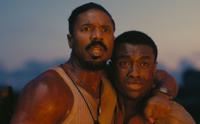 Two men hold each other in fear as they see an unknown threat in Sinners