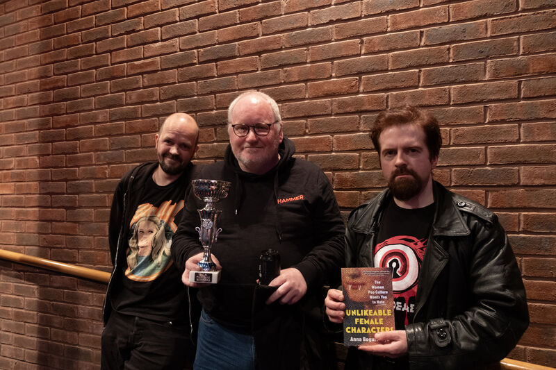 Three people holding prizes and the Dundead Quoz trophy