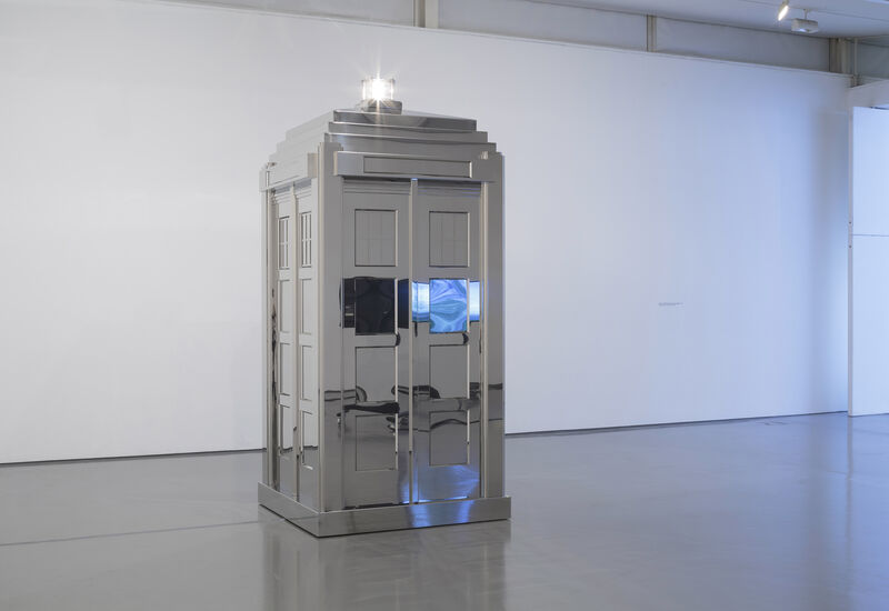 An old fashioned police box stands in the gallery space, painted in mirror paint, with a bright white light on top. 