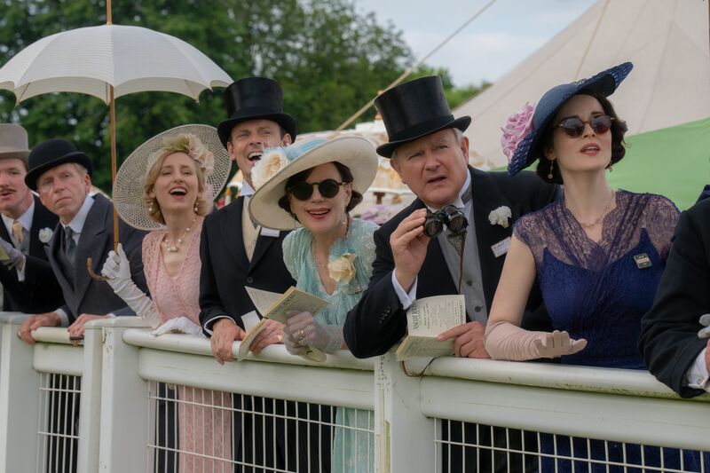 A group of people in formal, colourful dresses and tophats watch a race.