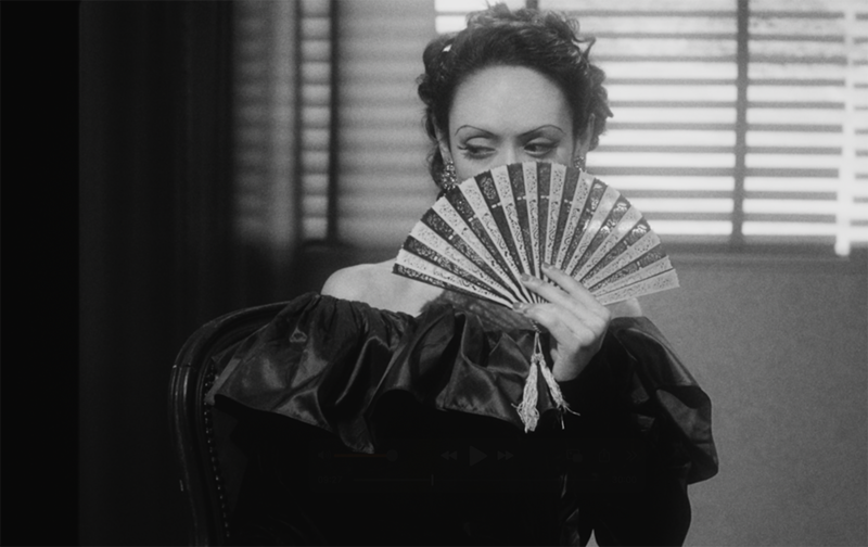 A woman looks from behind a fan
