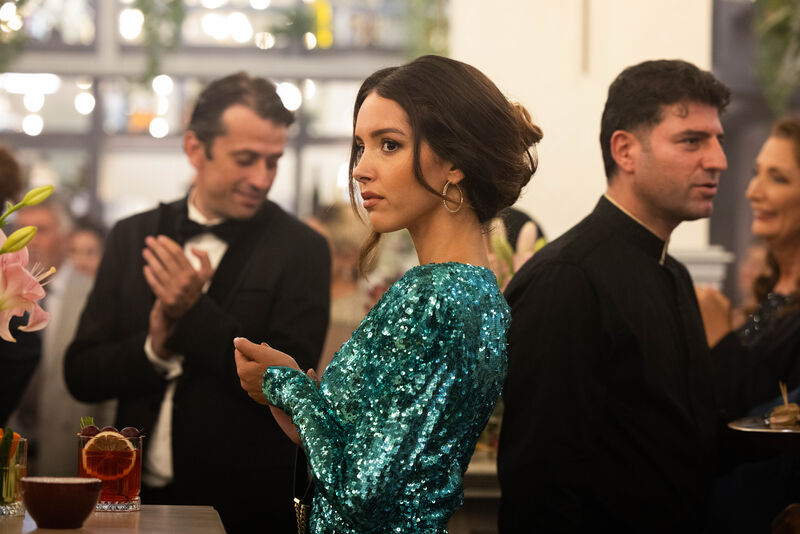 A women with a sparkly dress claps and looks to the side in a casino setting, men dressed in black are in the backgroud