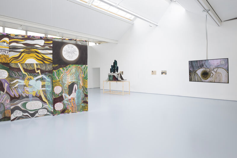 A hung textile work with watercolour painting and graphic text hangs to the left. A monitor hangs from the ceiling on the right. At the back is a plinth with a textile piece and on the back wall in the distance are two works on paper. The colours are muted and soft, the gallery is naturally lit and bright. 