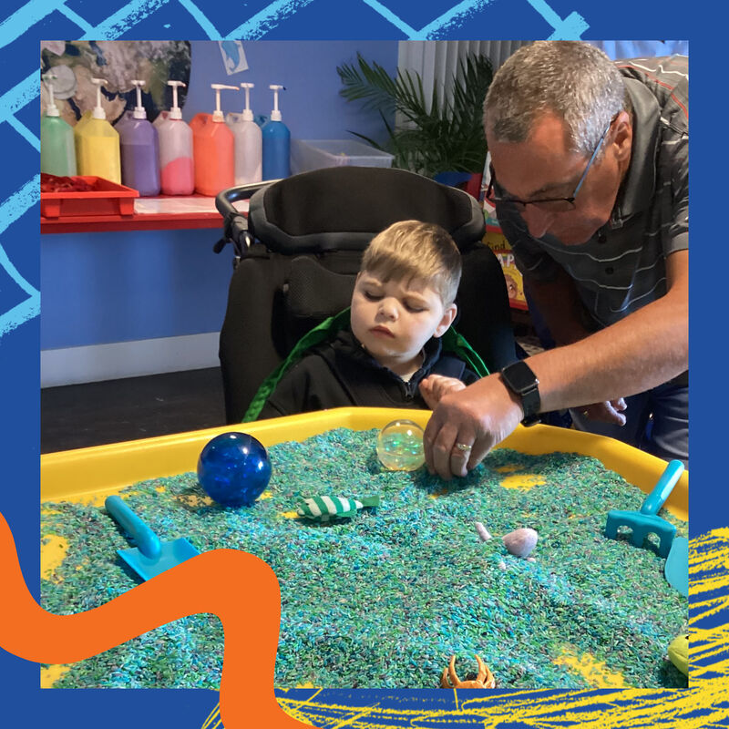 Child from Kingspark school looking at tub filled with colourful sand