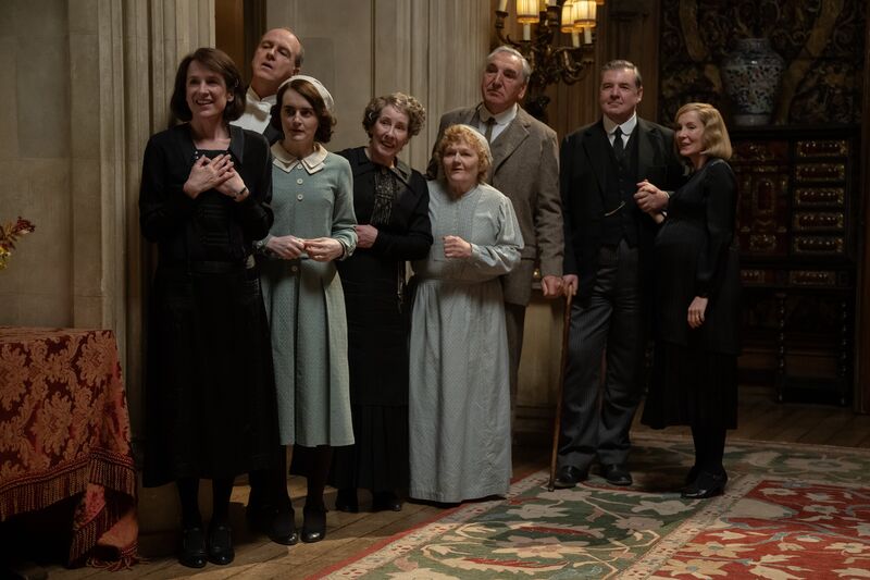 The cast of Downton Abbey stand watching and smiling.
