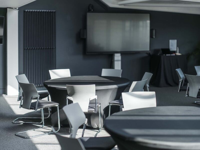 A room with circular tables and a screen on the wall 