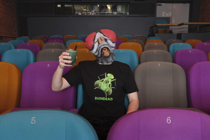 Person in DCA cinema wearing a fly mask, Dundead t-shirt and holding a green cocktail