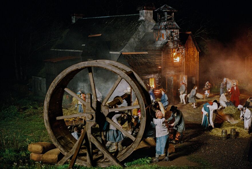 A group of villagers try to put out a burning barn using a water wheel.
