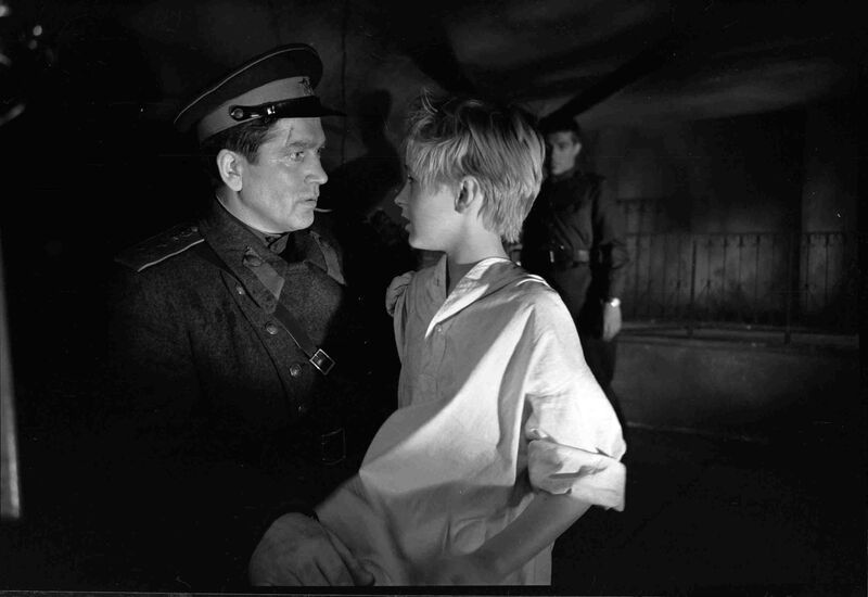 A boy and a soldier look at one another in a dark room