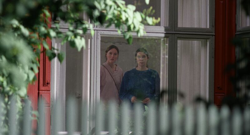 Two women look out of a window of a house